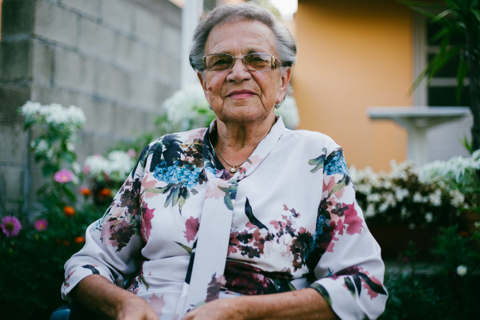 woman wearing white and multicolored floral top front of flower garden